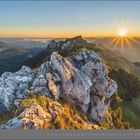 „08 | August“ zeigt eine felsige Berglandschaft bei Sonnenaufgang, mit leuchtenden Farben und strahlender Sonne im Hintergrund.