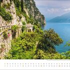 August. Kalender mit einer kurvigen Straße entlang steiler Felsen über einem See, umgeben von üppigem Grün.