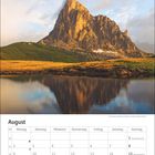 Augustkalender mit Wochen und Feiertagen. Im Hintergrund ein Berg mit See und Wolken im Abendlicht.