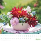 August, Kalender mit Blumenarrangement in Rot, Rosa und Blau in einer Schale auf einem Tisch im Freien.
