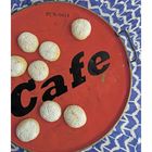Der Text sagt "PCN 0414" und "Cafe". Ein rotes Tablett mit Keksen auf einem blauen Tuch mit Zickzack-Muster.