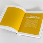 „PILATES: DIE GRUNDLAGEN“ steht linksbündig, darunter ein erklärender Text auf gelbem Hintergrund in einem Buch.