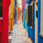 Kalender zeigt August 2027. Farbenfrohe enge Gasse mit bunt gestrichenen Häusern und flatternder Wäsche.