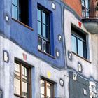 Kalenderseite für August 2021 mit einem farbenfrohen Gebäude, unregelmäßigen Fassaden und Balkonen mit Pflanzen.