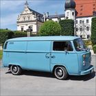 Ein hellblauer Lieferwagen steht vor einem historischen Gebäude mit Türmen und einem verzierten Tor.