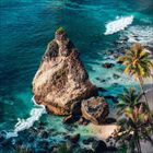 Keine sichtbaren Texte. Eine felsige Küste mit türkisfarbenem Wasser, großen Felsen und Palmen am Strand.