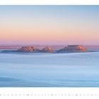 Augustkalender mit Landschaftsansicht, pastellfarbener Himmel und drei erodierte Hügel in einer weiten, flachen Ebene.