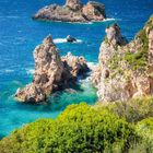 Kalender im August. Felsküste bei Paleokastritsa, Korfu. Klare See, grüne Büsche, steile, felsige Klippen.