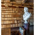 07 FEBRUAR. Eine historische Bibliothek mit Bücherregalen, einer Marmorbüste, reich verzierten Decken und einem Sessel.