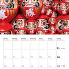 Kalenderblatt: August 2027, Wochenbeginn Montag. Hintergrund zeigt viele rote Daruma-Puppen mit weißen japanischen Schriftzeichen.