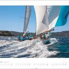 August: Kalender mit einem Segelboot auf rauer See. Crew in blauen Hemden, Segel gebläht, Küstenlandschaft im Hintergrund.