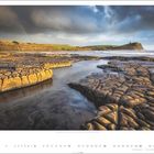 Kimmeridge Bay, Jurassic Coast, Dorset. Küste mit flachem Felsen im Vordergrund, grüne Hügel und Regenbogen im Hintergrund.