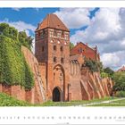 „8“, „Tangermünde, Sachsen-Anhalt“. Historisches rotes Backsteingebäude mit Türmen und Zinnen, umgeben von grünen Pflanzen.