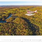 Text: "Indian Summer in Mauricie, Québec." Ein rotes Wasserflugzeug fliegt über einen herbstlichen Wald mit Seen.