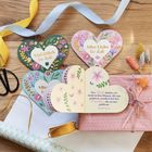 Herzförmige Karten mit Texten "Viel Glück für dich" und "Alles Liebe für dich" auf einem Holztisch mit Bändern und Blumen.