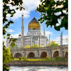 Kalenderblatt für August mit Nummern und Wochentagen. Blick durch Bäume auf Gebäude mit Kuppel und Minarett.