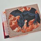 "ZEIG KEINE..." steht auf einem Buchrücken. Es zeigt einen schwarzen Drachen auf orangefarbenem Hintergrund mit Verzierungen.