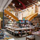 Schilder mit "religion", "pays", "université". Helle Buchhandlung mit vielen Büchern, gelbes Treppengeländer führt nach oben.