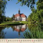 08. Kalender mit August-Daten; Schloss mit rotem Dach spiegelt sich in ruhigem See, umgeben von Bäumen und Natur.