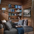 Ein gemütlicher Raum mit Holzwänden, grauen Sofakissen, einem Bücherregal und einer gerahmten Schwarz-Weiß-Fotografie.