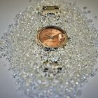 Uhr mit goldfarbener Oberfläche und römischen Ziffern, umgeben von glitzernden, kleinen Diamanten.