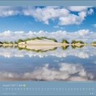 August 2027. Eine Dünenlandschaft spiegelt sich im Wasser, umgeben von Wolken und blauem Himmel.