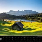 Alpen 08: Geroldsee mit Karwendelgebirge. Grüne Wiesen, Hütten, See und Berge bei klarem Himmel im Hintergrund.