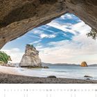 08. Kalender mit Strandansicht durch Felsenöffnung, Meer, Felsformationen in der Ferne, blauer Himmel mit dünnen Wolken.