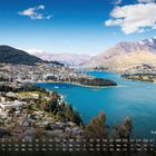 „Queenstown 8“ unten. Blick auf eine Stadt am türkisfarbenen See, umgeben von Bergen und Wald.