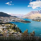 Text: "Queenstown 8". Unten ein Monatskalender. Blick auf Stadt, blauen See, grüne Hügel und schneebedeckte Berge.