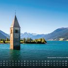 Kalender mit einem versunkenen Kirchturm im Reschensee, umgeben von Bergen und klarem Wasser.