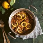 Zitronen-Hähnchengericht in einer Pfanne, garniert mit Zitronenscheiben, auf einem dunklen Tisch mit frischen Zitronen.