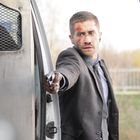 Ein Mann im Anzug mit blutverschmiertem Gesicht zielt mit einer Pistole aus einem offenen Transporter.