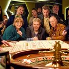 Mehrere Menschen versammelt um einen Roulettetisch, gespannt in Erwartung des Ergebnisses. Viel Neugier und Spannung.