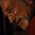 Ein älterer Mann mit Schnurrbart lächelt seitlich, er trägt ein rotes Oberteil.