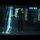 Kein erkennbarer Text. Eine Frau steht schreiend in einem verlassenen, dunklen Raum, durch den Lichtstrahlen fallen.