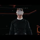 Person in dunkler Kleidung und VR-Headset vor schwarzem, geometrisch gemustertem Hintergrund mit roten und grauen Linien.