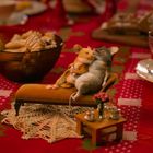 Zwei Mäuse liegen auf einer Miniatur-Couch, umgeben von Keksen und Süßigkeiten auf einem festlichen Tisch.