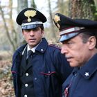 Zwei Personen in blauen Uniformen mit Mützen und goldenen Insignien stehen im Wald. Sie scheinen in ein Gespräch vertieft.