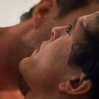 Zwei Personen eng umschlungen, eine liegt mit dem Kopf zurück, Hautkontakt und Nähe sind im Fokus.