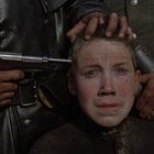 Ein ängstlicher Junge wird an den Haaren gehalten, eine Pistole an seinen Kopf gerichtet.