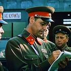 Text "НЕ КУРИТЬ" auf Schild. Drei Männer in sowjetischen Militäruniformen, einer schreibt in ein Notizbuch.