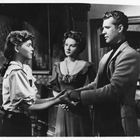 Drei Personen stehen in einem Raum. Zwei Frauen und ein Mann reichen sich die Hände. Die Kleidung wirkt historisch.