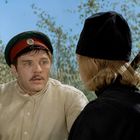 Es gibt keinen Text. Ein Mann in Uniform schaut überrascht, daneben ein anderer mit schwarzem Hut, umgeben von Bäumen.
