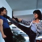 Ein Mann in blauem Shirt wird von einer Frau in gestreifter Bluse mit einem hohen Tritt gegen die Wand gedrückt.