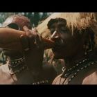 Drei Personen, traditionell gekleidet, eine trinkt aus einem Behälter. Hintergrund mit Bäumen.
