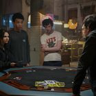 Ein Mann trägt ein T-Shirt mit der Aufschrift "LET'S". Vier Personen stehen um einen runden Tisch mit Pokerchips.