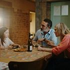 Eine Familie sitzt am Esstisch, redet und genießt eine Mahlzeit. Durch das Fenster strahlt Sonnenlicht.