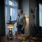 Ein Mann in Uniform steht an einem Fenster. Er schaut hinaus, umgeben von Möbeln und Dekorationen.