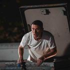 Ein Mann in weißem T-Shirt klettert aus einer dunkelgrauen, offenen Dachluke und hält etwas in der Hand.